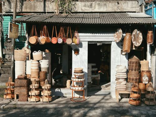 A traditional Balinese street shop displaying a variety of handwoven baskets and local crafts in front of its grey facade under a clear sky.